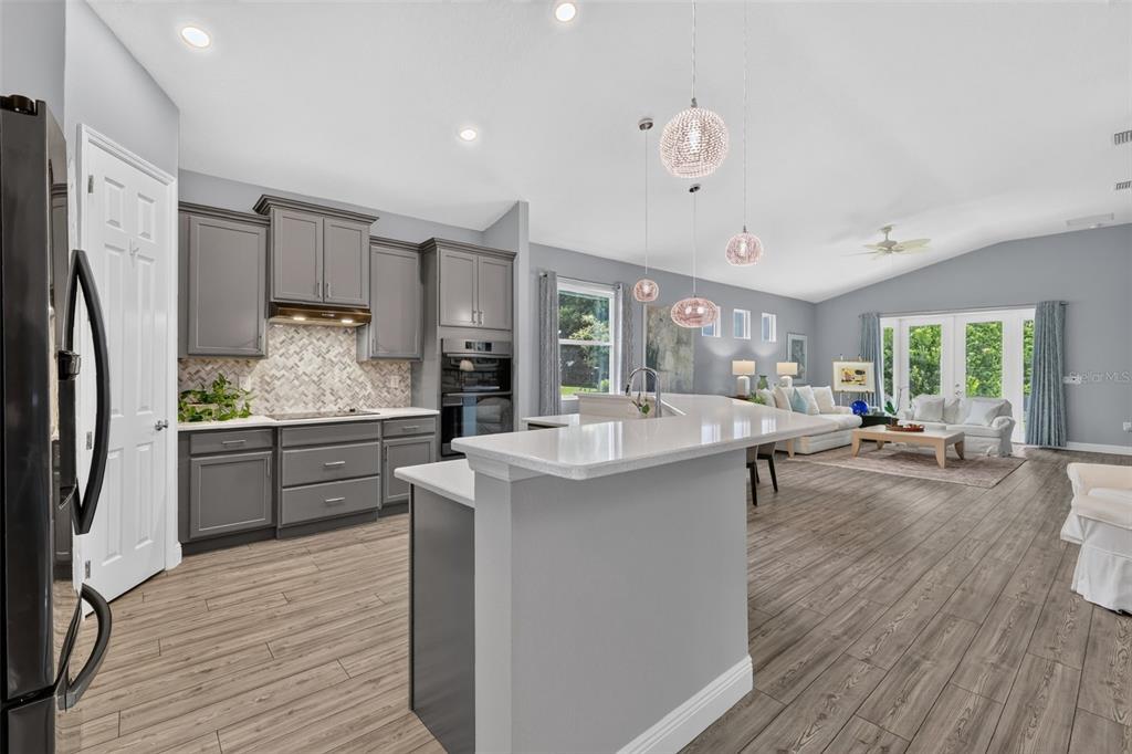 A spacious living room with gray walls, wood-look flooring, a white sofa, and an open kitchen — 8220 BRIDGEPORT BAY CIRCLE, MOUNT DORA, FL