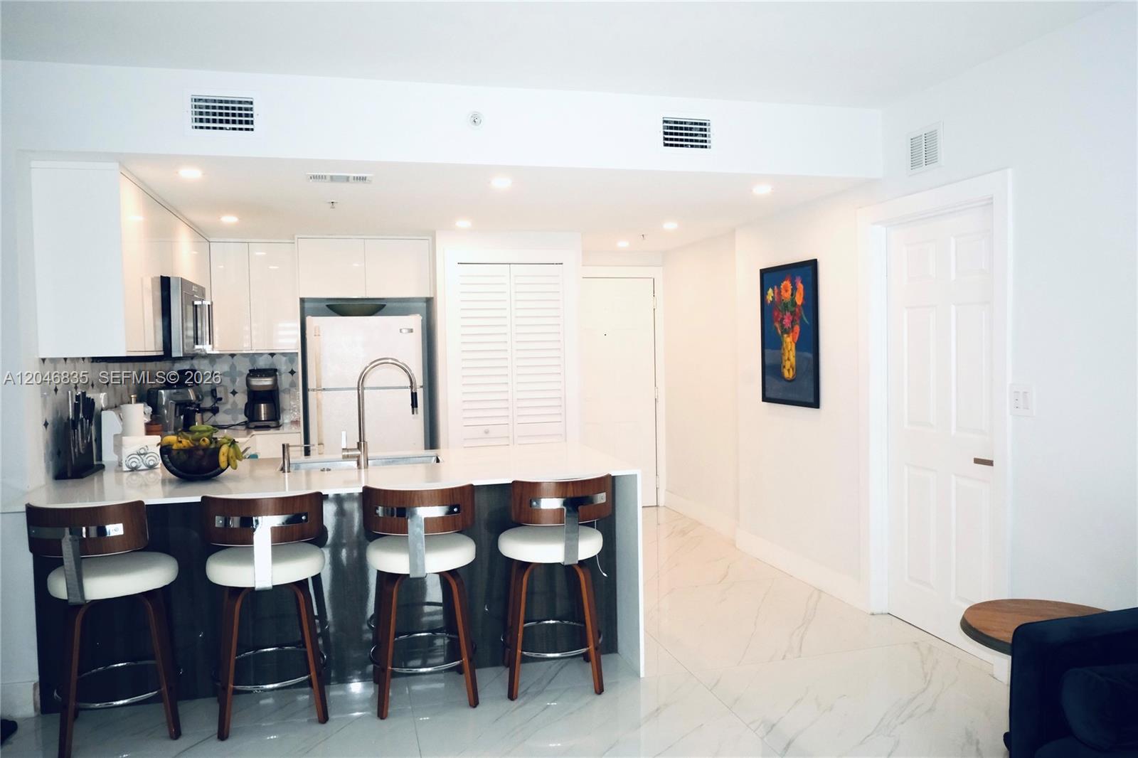 A modern kitchen features white cabinetry, a waterfall island with bar stools, and marble flooring — 3410 Coral Way # 05, Miami FL 33145, MIAMI, FL