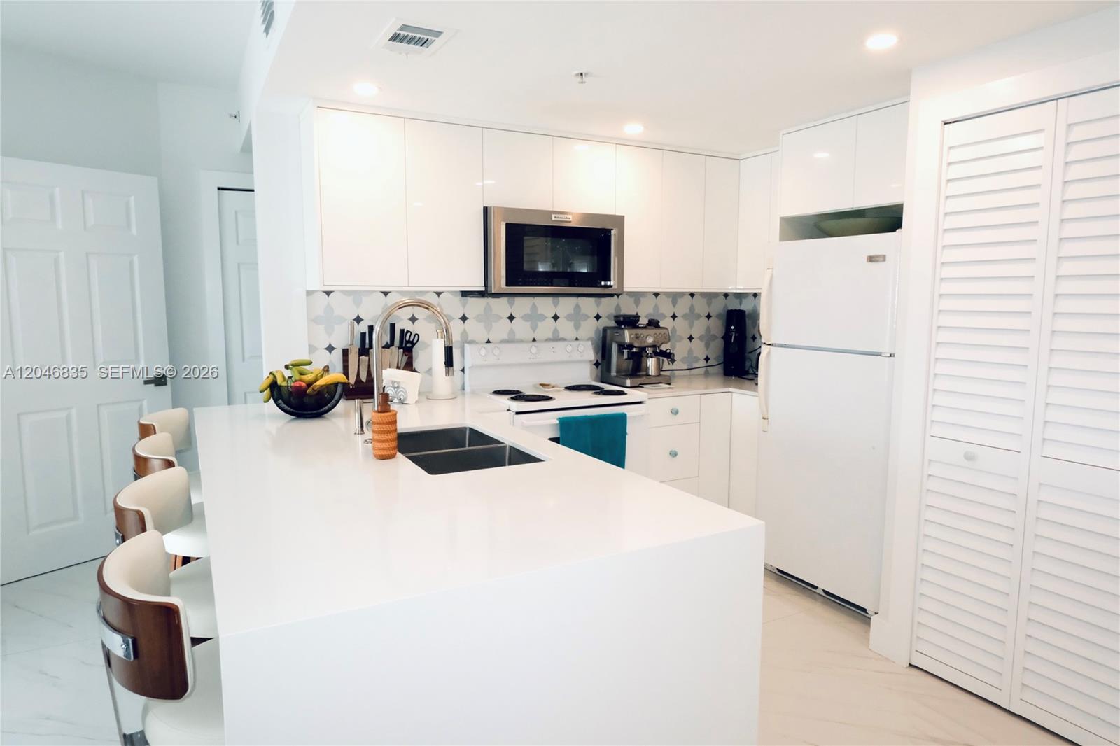 A modern kitchen features white cabinetry, a large island with a sink, and patterned backsplash — 3410 Coral Way # 05, Miami FL 33145, MIAMI, FL