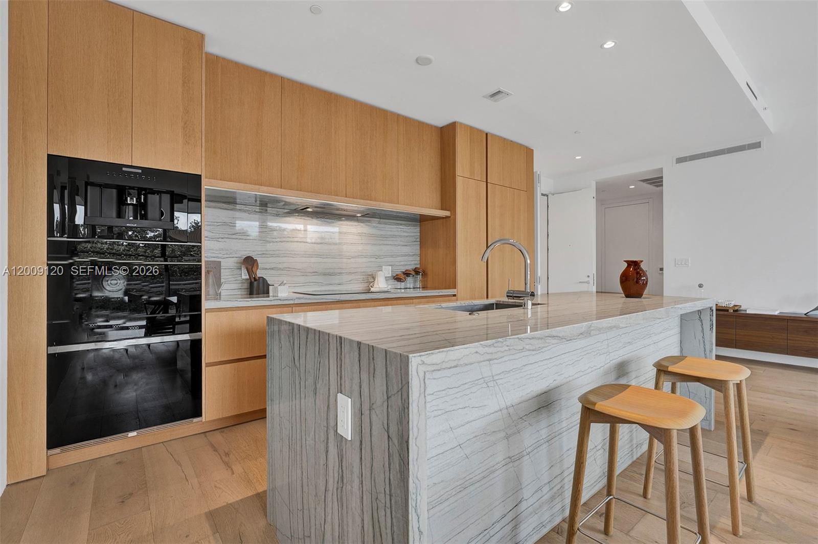 A modern kitchen features light wood cabinetry, a stone waterfall island, and integrated appliances — 8701 Collins Ave # 304, Miami Beach FL 33154, MIAMI BEACH, FL