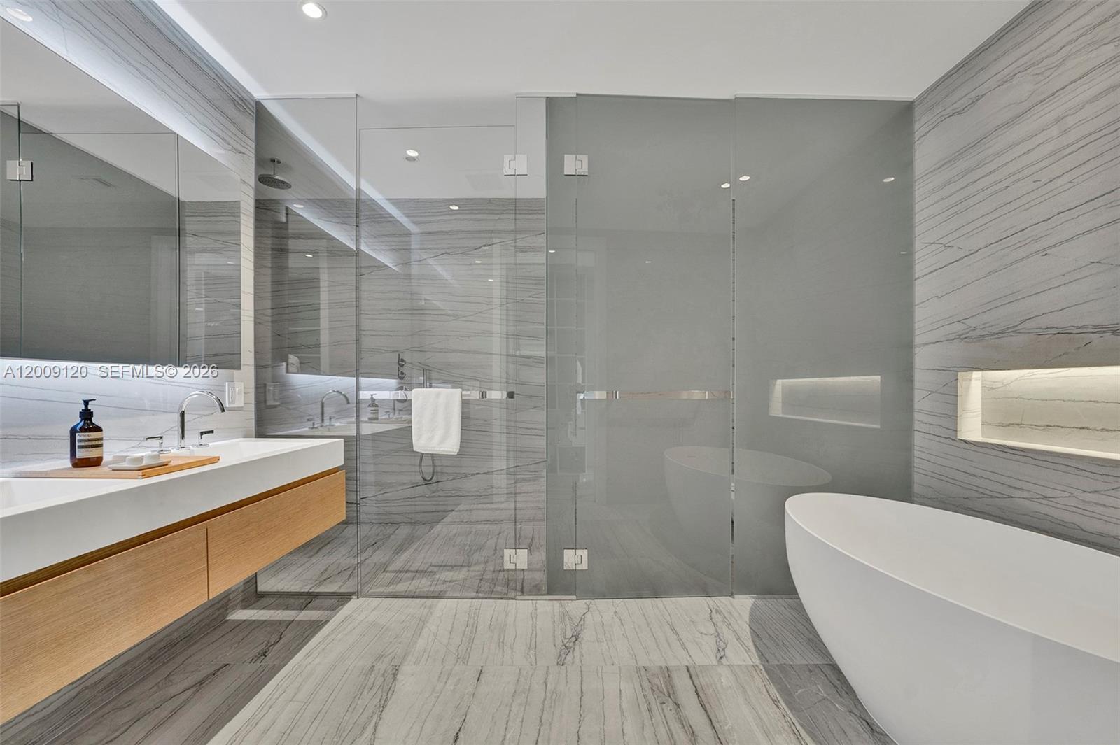 A modern bathroom features a floating wood vanity, a glass-enclosed shower, and a freestanding tub — 8701 Collins Ave # 304, Miami Beach FL 33154, MIAMI BEACH, FL