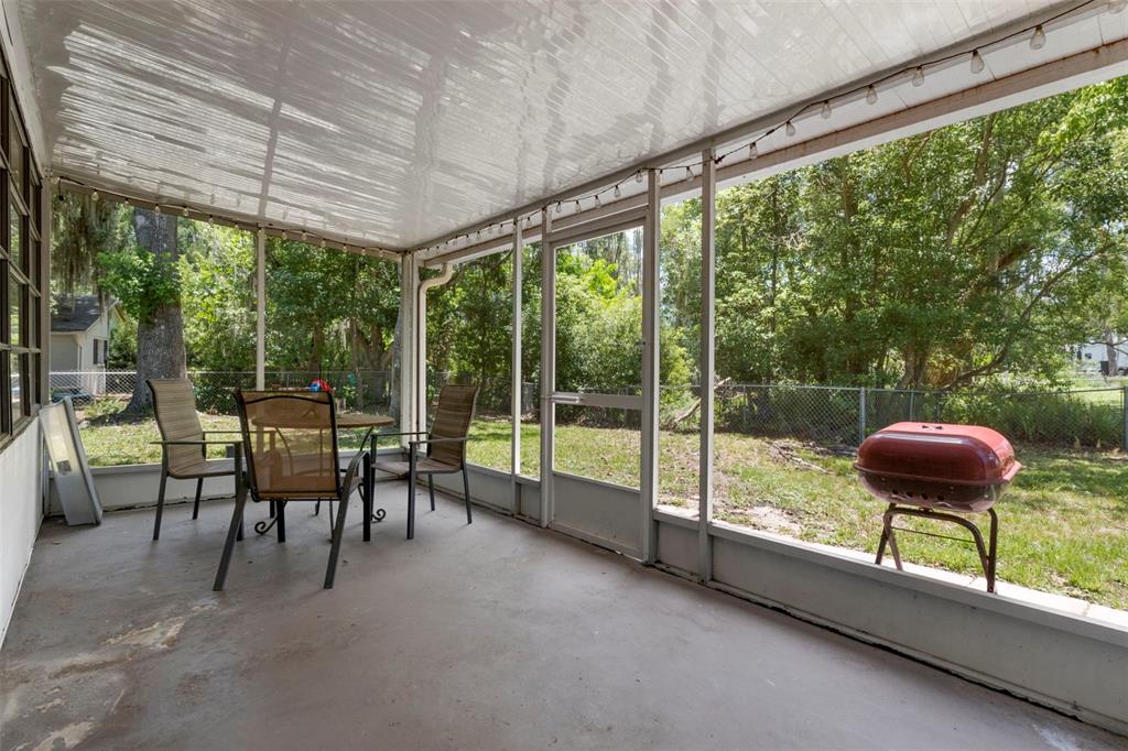 A screened-in porch with a concrete floor, patio furniture, and a red charcoal grill — 4737 KING LAKE DRIVE, LAND O LAKES, FL
