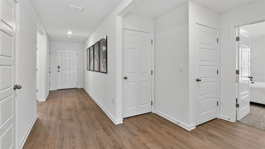 A hallway with wood-look flooring leads to a front door with several white interior doors — 70 BRIDGEHAVEN DRIVE, PALM COAST, FL