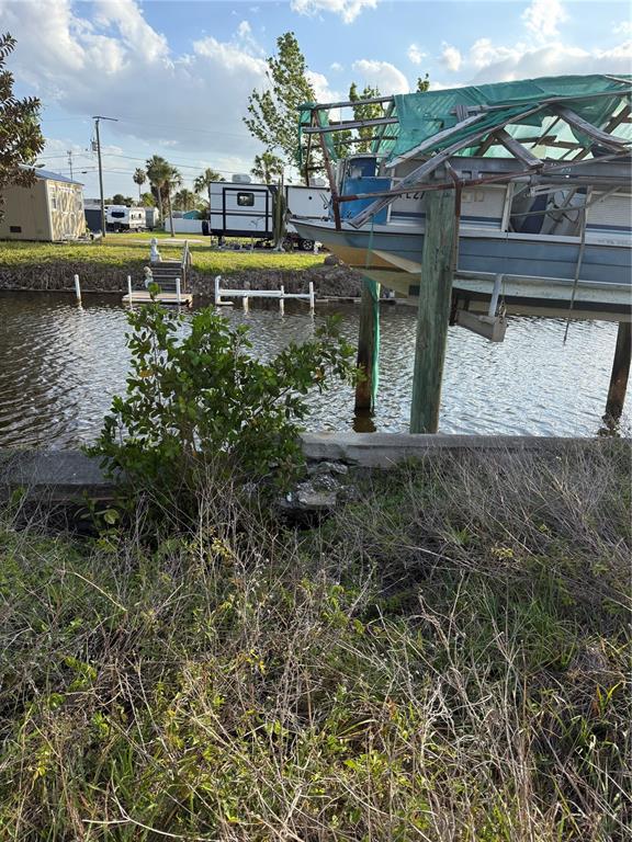 A boat on a lift sits above a canal next to a grassy waterfront lot — 4153 HOLLIS AVENUE, PORT CHARLOTTE, FL
