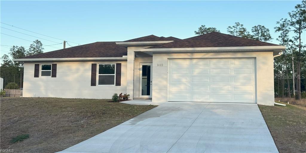 A single-story house with a white stucco exterior, dark shutters, and a two-car garage — 1422 HIGHLAND AVENUE, LEHIGH ACRES, FL