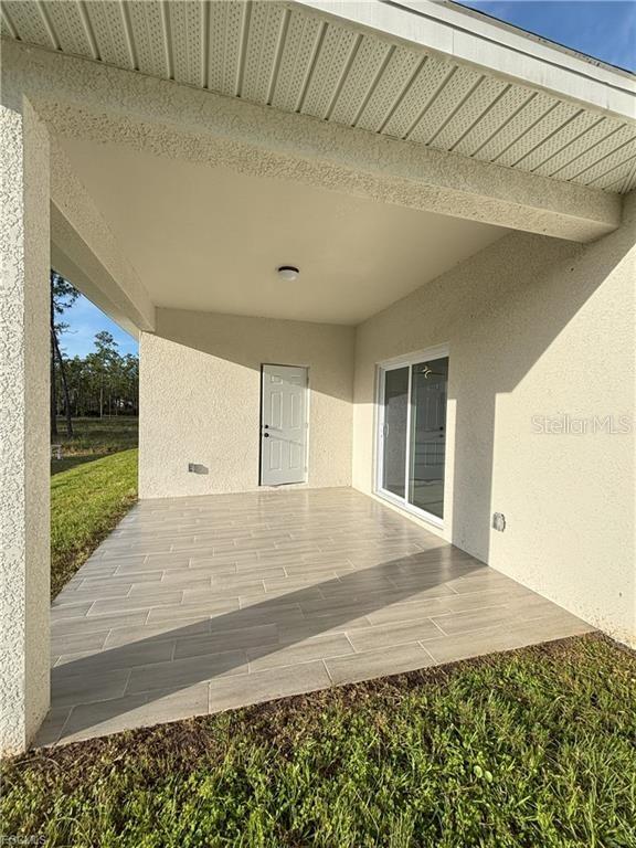 A covered patio features light-colored tile flooring, a single door, and a sliding glass door — 1422 HIGHLAND AVENUE, LEHIGH ACRES, FL