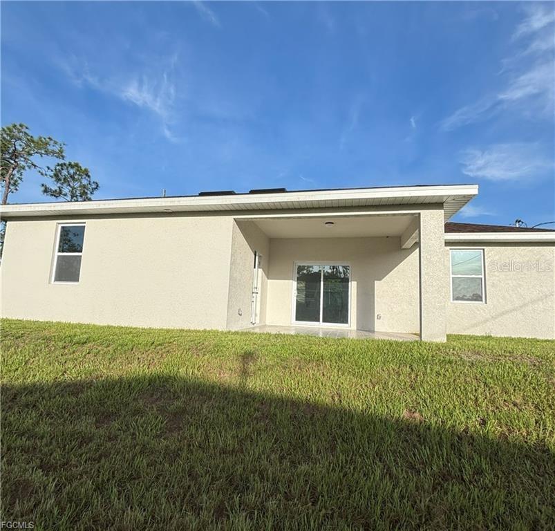 The rear exterior of a single-story house features a covered patio and sliding glass doors — 1422 HIGHLAND AVENUE, LEHIGH ACRES, FL
