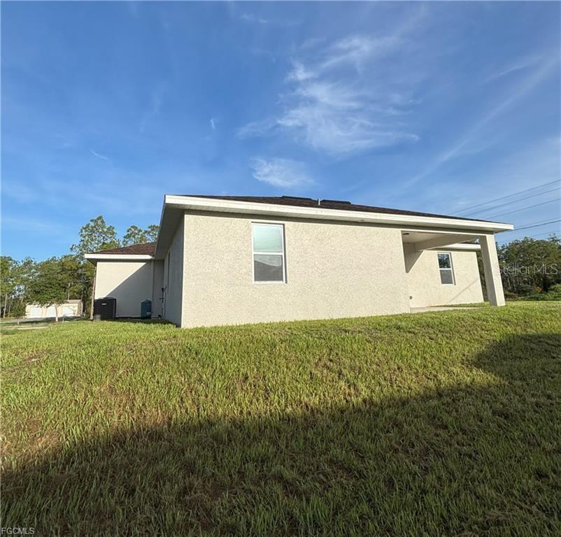 The exterior of a beige stucco house features a covered patio and a grassy yard — 1422 HIGHLAND AVENUE, LEHIGH ACRES, FL