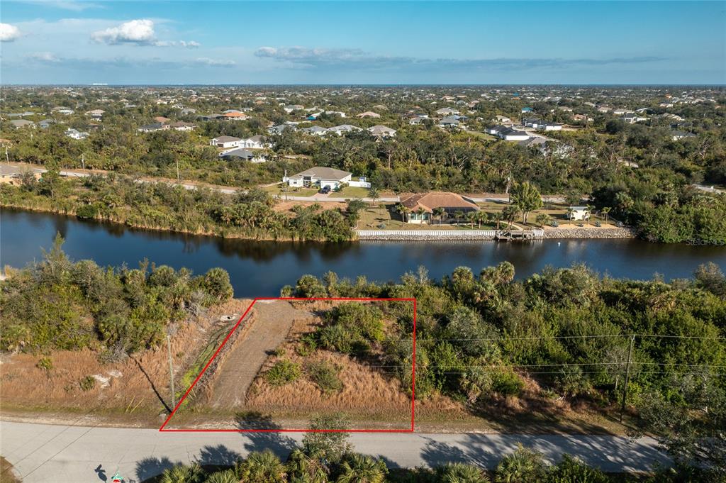 An aerial view shows a vacant, rectangular lot with a dirt driveway bordering a canal — 10136 COCOA BEACH STREET, PORT CHARLOTTE, FL