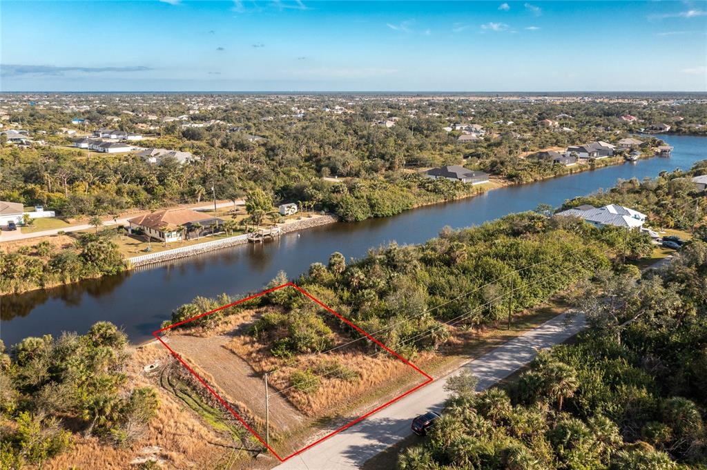 An aerial view shows a vacant, rectangular waterfront lot outlined in red next to a road — 10136 COCOA BEACH STREET, PORT CHARLOTTE, FL