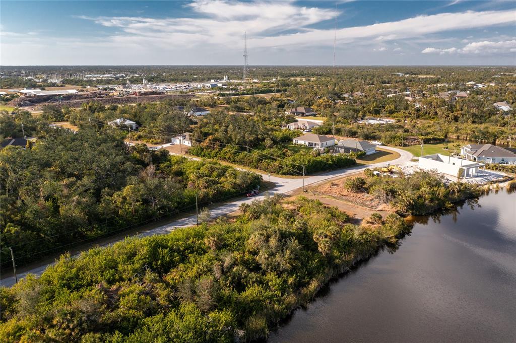 An aerial view shows a residential street, wooded lots, and a pond under a blue sky — 10136 COCOA BEACH STREET, PORT CHARLOTTE, FL