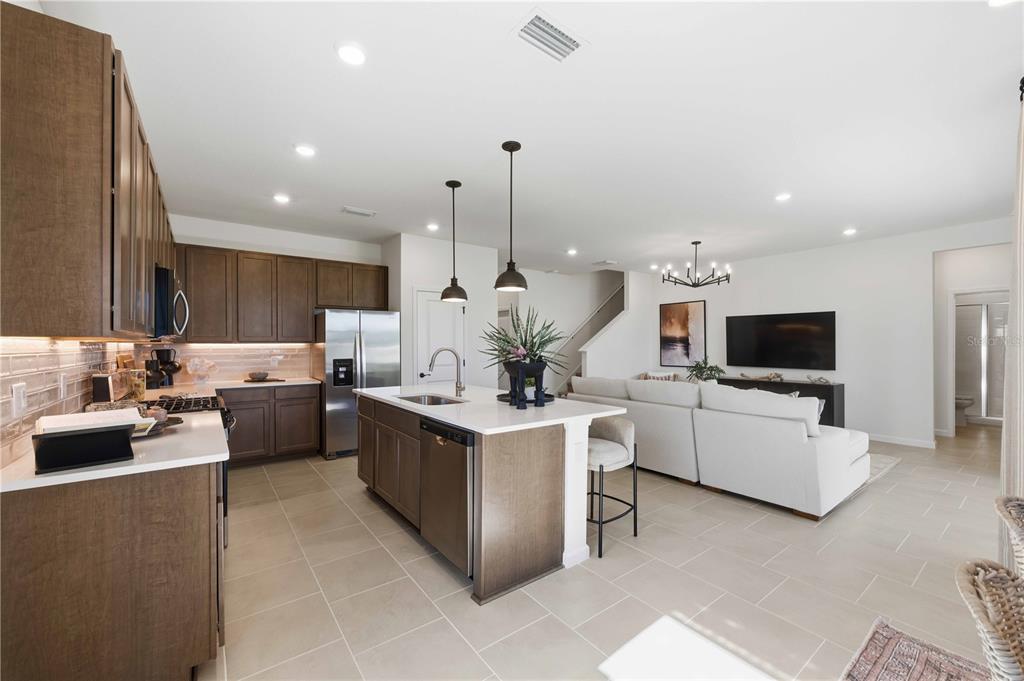 A modern kitchen with dark wood cabinets and a white island opens to a living room — 10653 NW SUNCREST LOOP, PORT ST LUCIE, FL