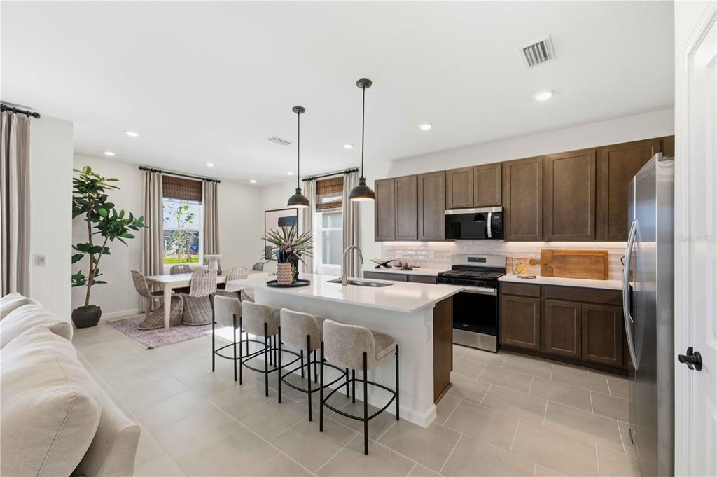 A kitchen with dark wood cabinets, a white island with seating, and an adjacent dining area — 10653 NW SUNCREST LOOP, PORT ST LUCIE, FL