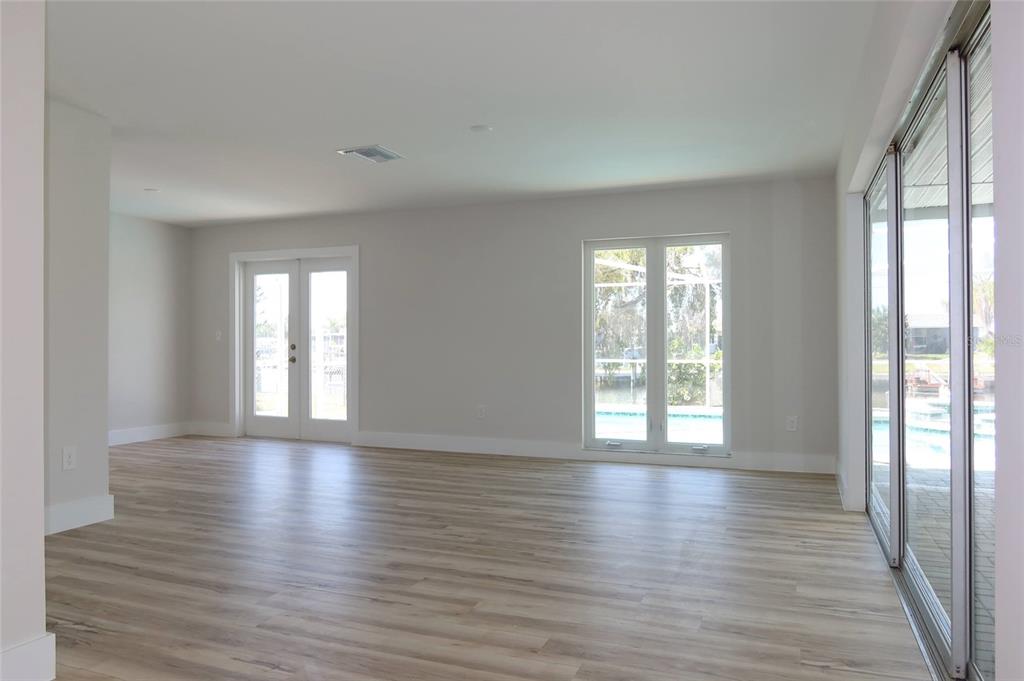 An empty room with light wood-look flooring, white walls, French doors, and sliding glass doors — 4240 FLORAMAR TERRACE, NEW PORT RICHEY, FL