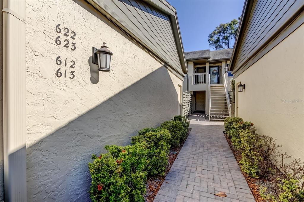 A paved walkway leads between two stucco buildings toward an outdoor staircase and upper balcony — 3163 LANDMARK DRIVE UNIT 623, CLEARWATER, FL