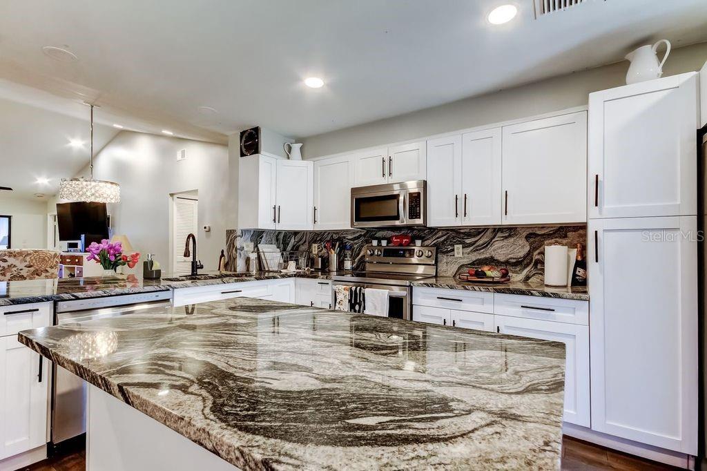 A kitchen features white cabinets, stainless steel appliances, and a large, dark patterned granite island — 3163 LANDMARK DRIVE UNIT 623, CLEARWATER, FL