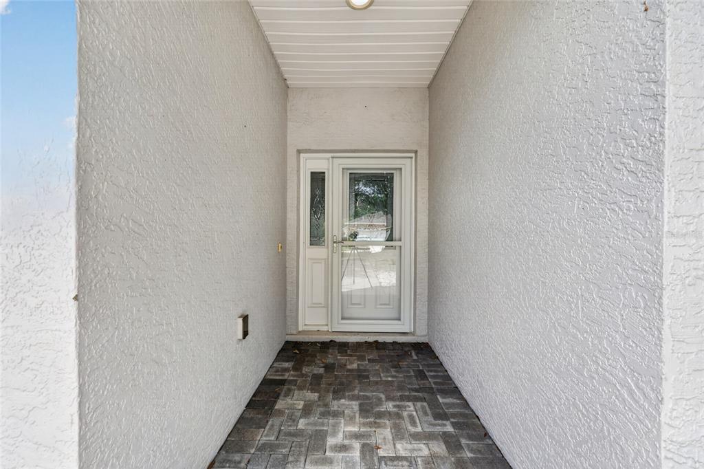 A covered entryway features a paved floor, textured white walls, and a glass storm door — 7933 SW 83RD PLACE, OCALA, FL