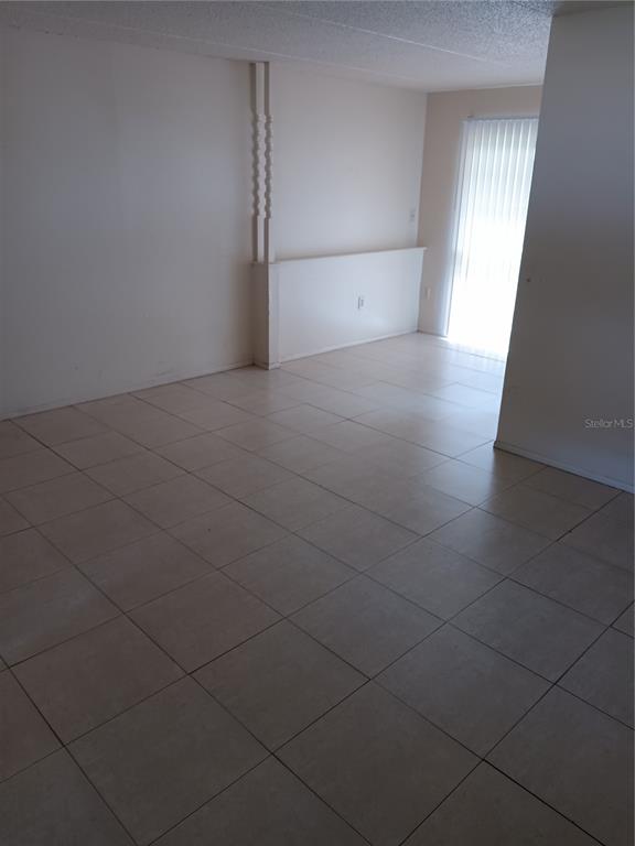 An empty room features light-colored floor tiles, white walls, and a sliding glass door — 1906 HONOUR ROAD UNIT 2, ORLANDO, FL