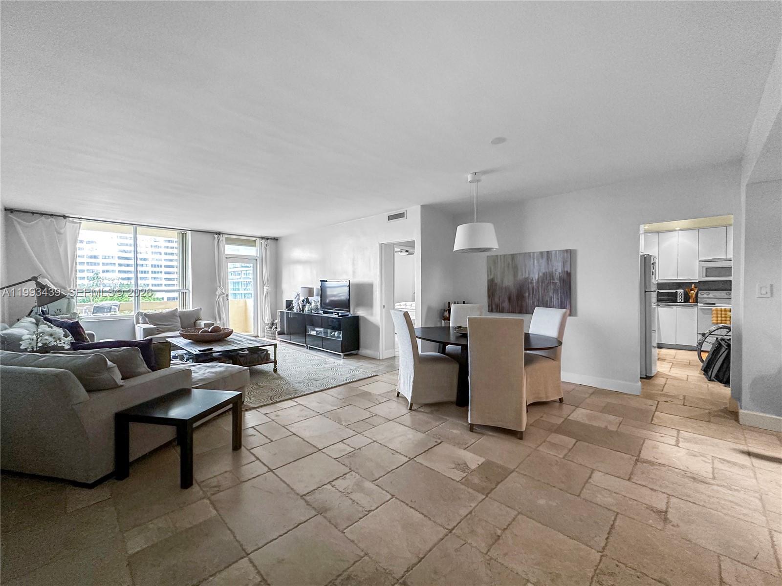 An open-concept living and dining area features stone tile flooring and a view of buildings — 10185 Collins Ave # 502, Bal Harbour FL 33154, BAL HARBOUR, FL