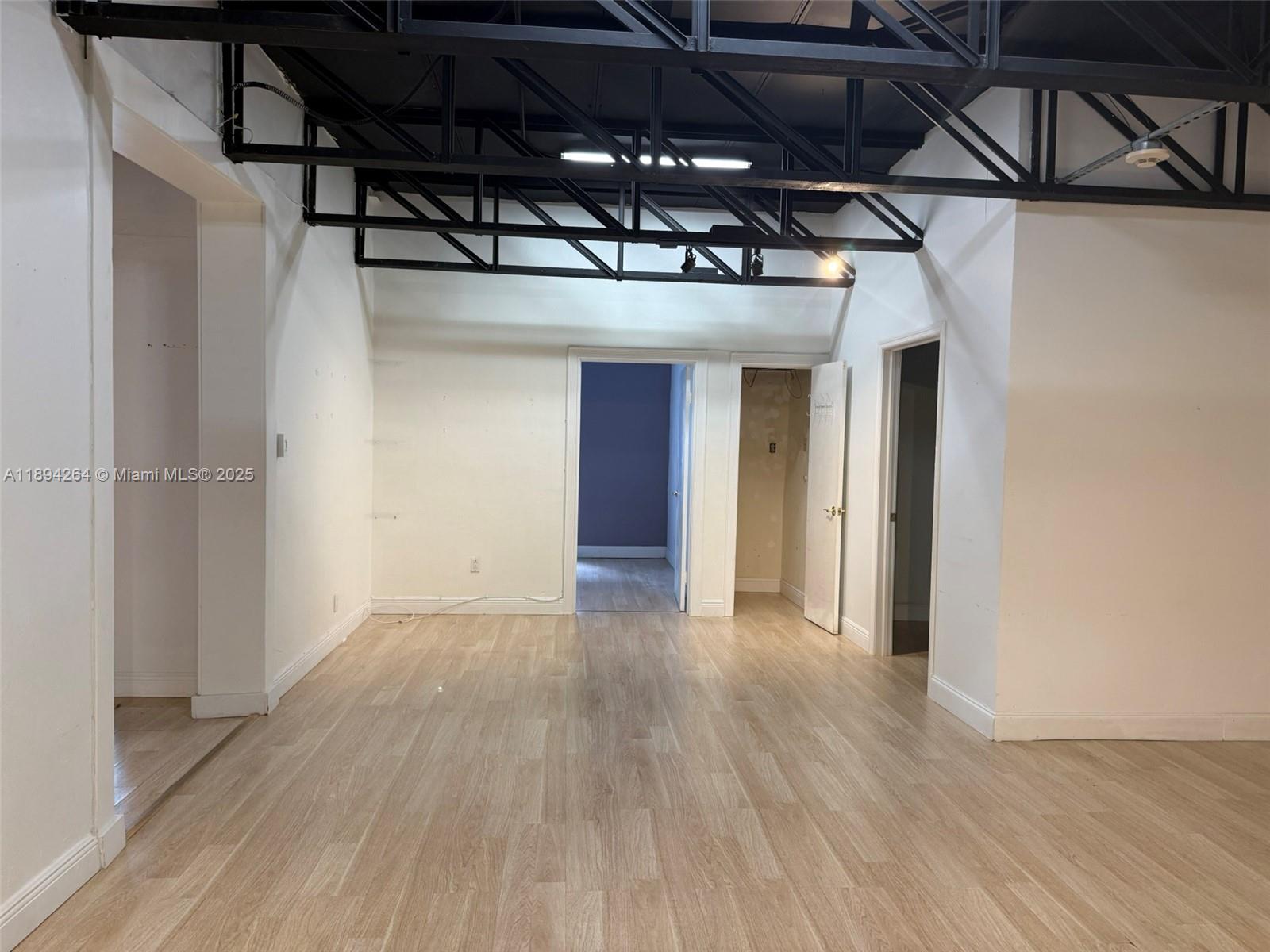 An interior room features light wood-look flooring, white walls, and an exposed black metal ceiling — 299 Alhambra Cir, Coral Gables FL 33134, CORAL GABLES, FL