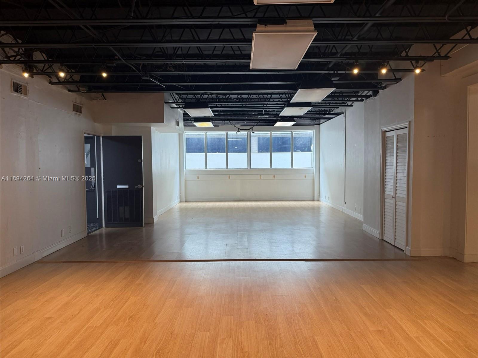 An empty commercial space features wood-look flooring, white walls, and an exposed black ceiling — 299 Alhambra Cir, Coral Gables FL 33134, CORAL GABLES, FL