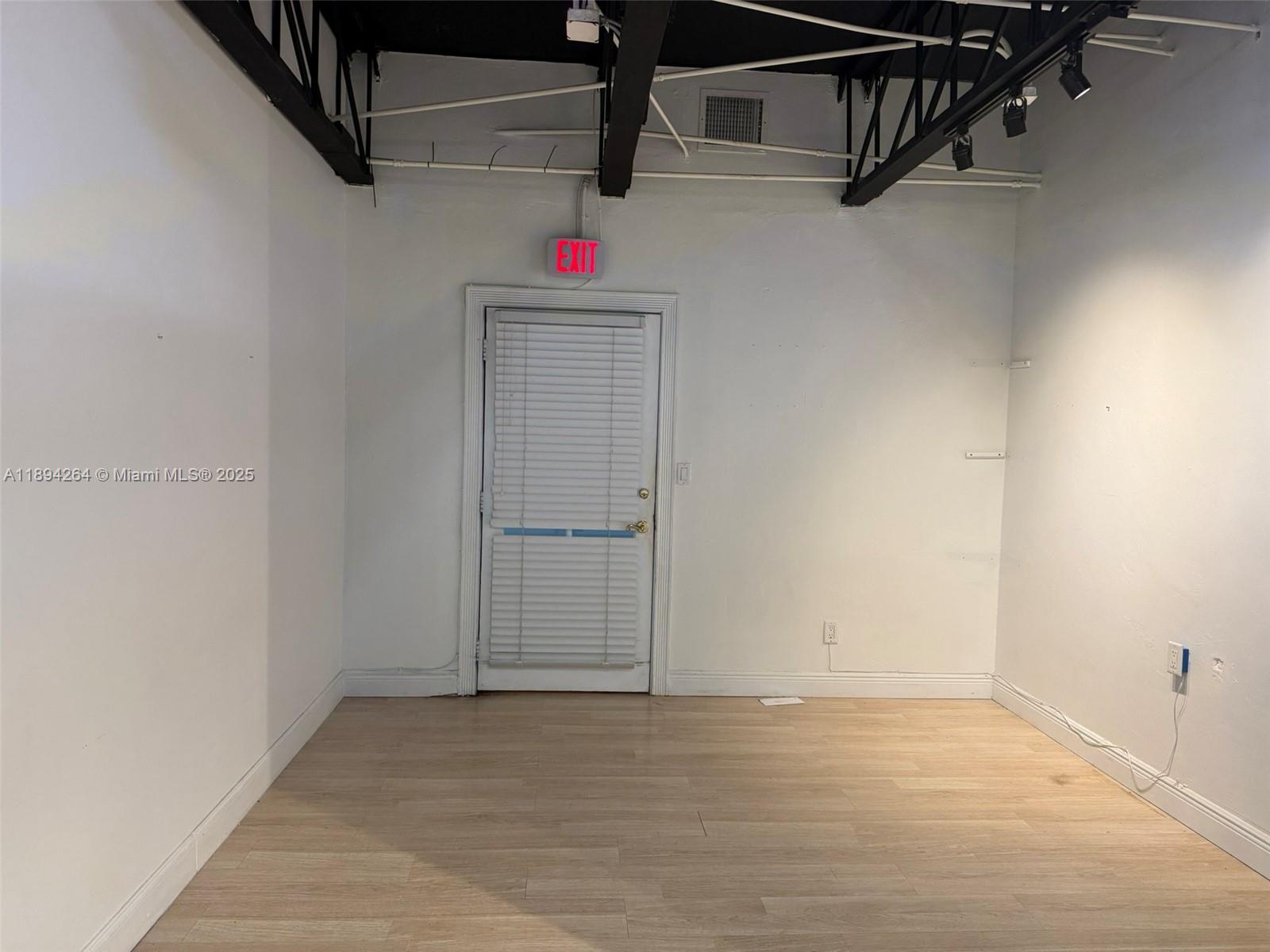 An empty room features white walls, light wood-look flooring, and an exposed black ceiling structure — 299 Alhambra Cir, Coral Gables FL 33134, CORAL GABLES, FL