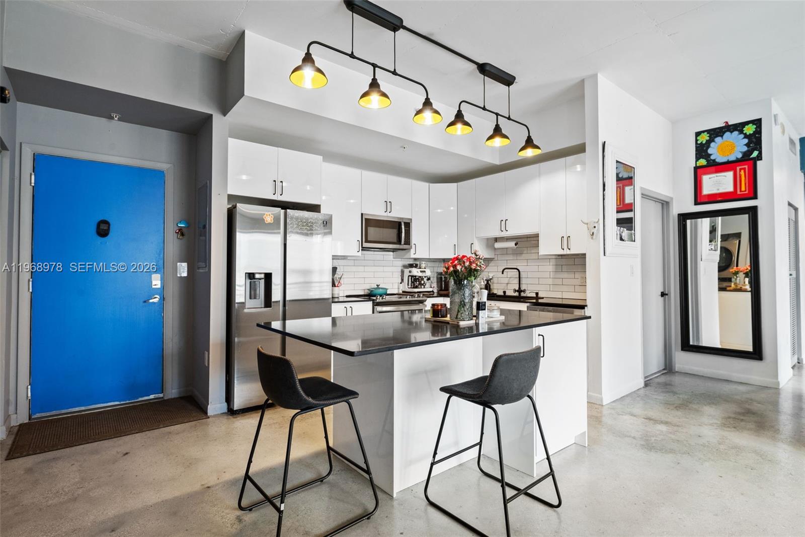 A modern kitchen features white cabinets, a black island with two stools, and industrial lighting — 133 NE 2nd Ave # 1606, Miami FL 33132, MIAMI, FL