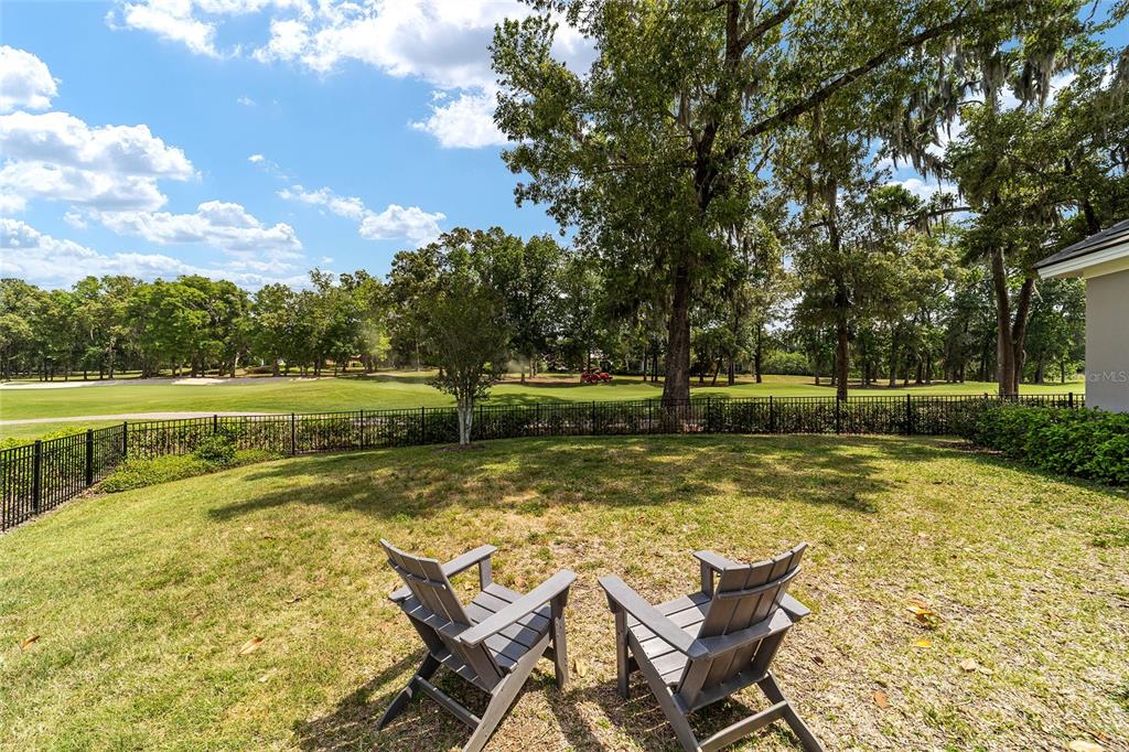 Two gray Adirondack chairs sit on a grassy backyard lawn overlooking a golf course — 7554 NW 33RD PLACE, OCALA, FL