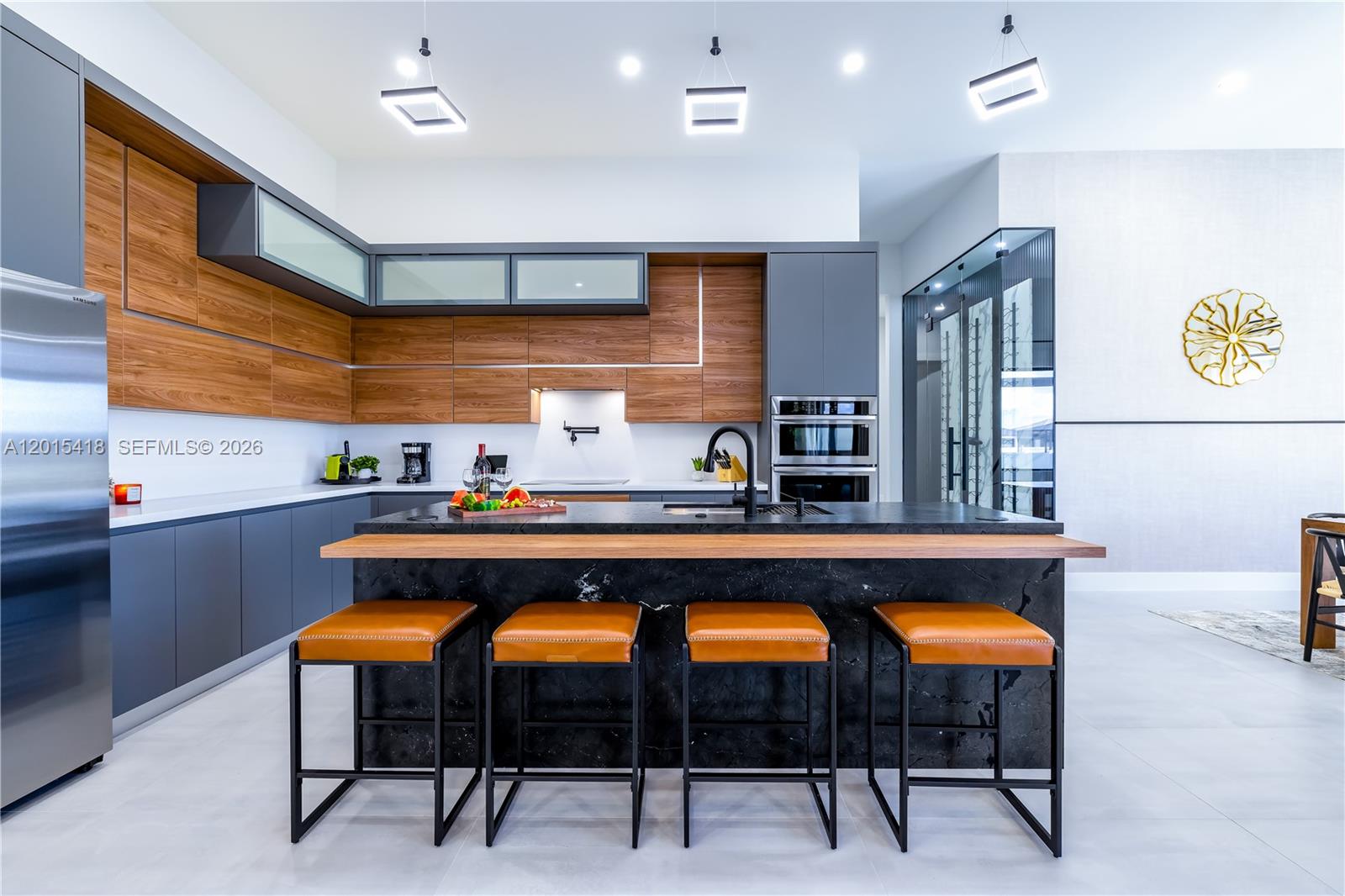 A modern kitchen features dark cabinetry, wood-grain accents, a black marble island, and four barstools — 10 SW 33rd PL, Cape Coral FL 33904, CAPE CORAL, FL