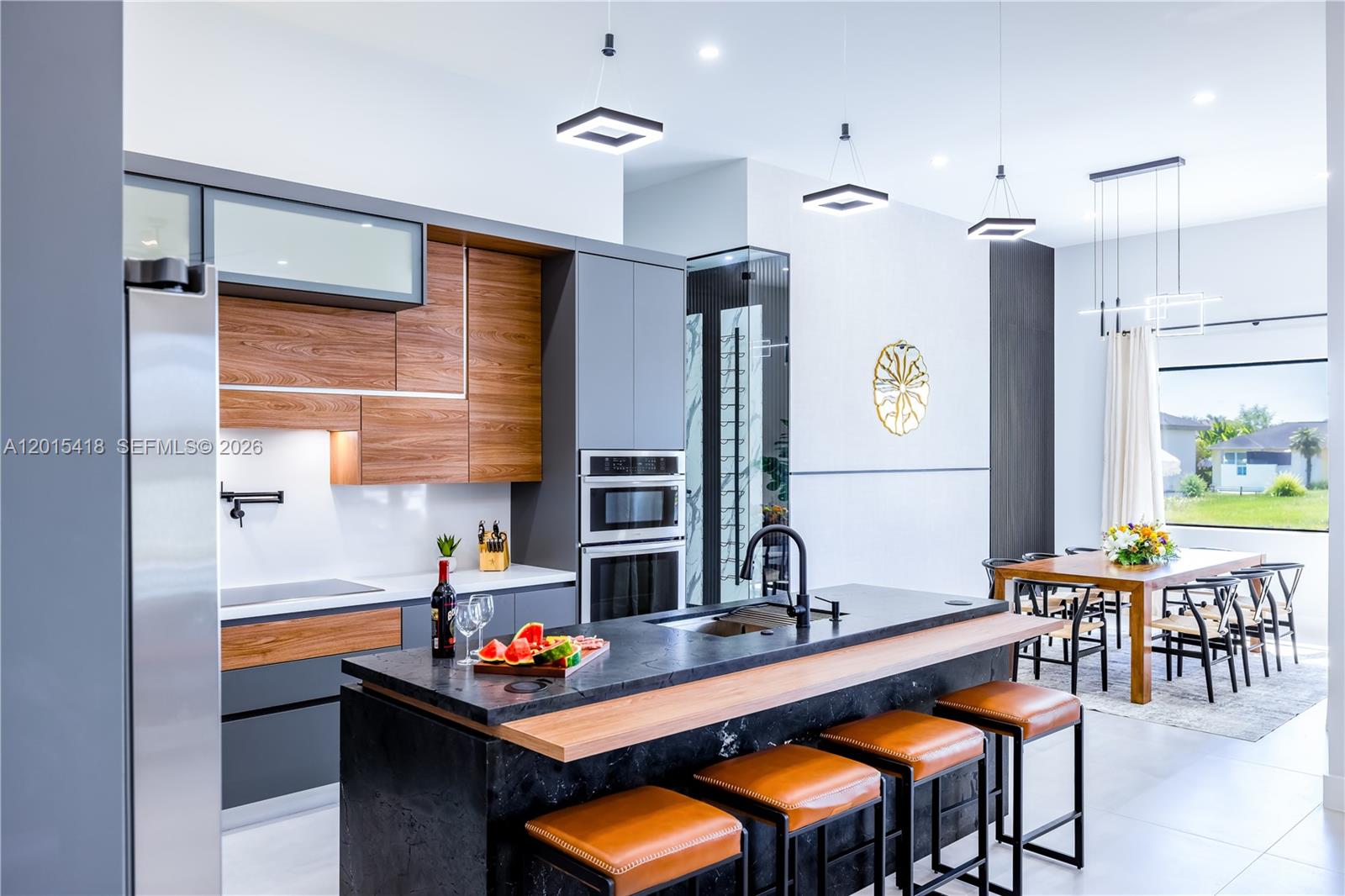 A modern kitchen features dark stone countertops, wood-accented cabinetry, and a central island with stools — 10 SW 33rd PL, Cape Coral FL 33904, CAPE CORAL, FL