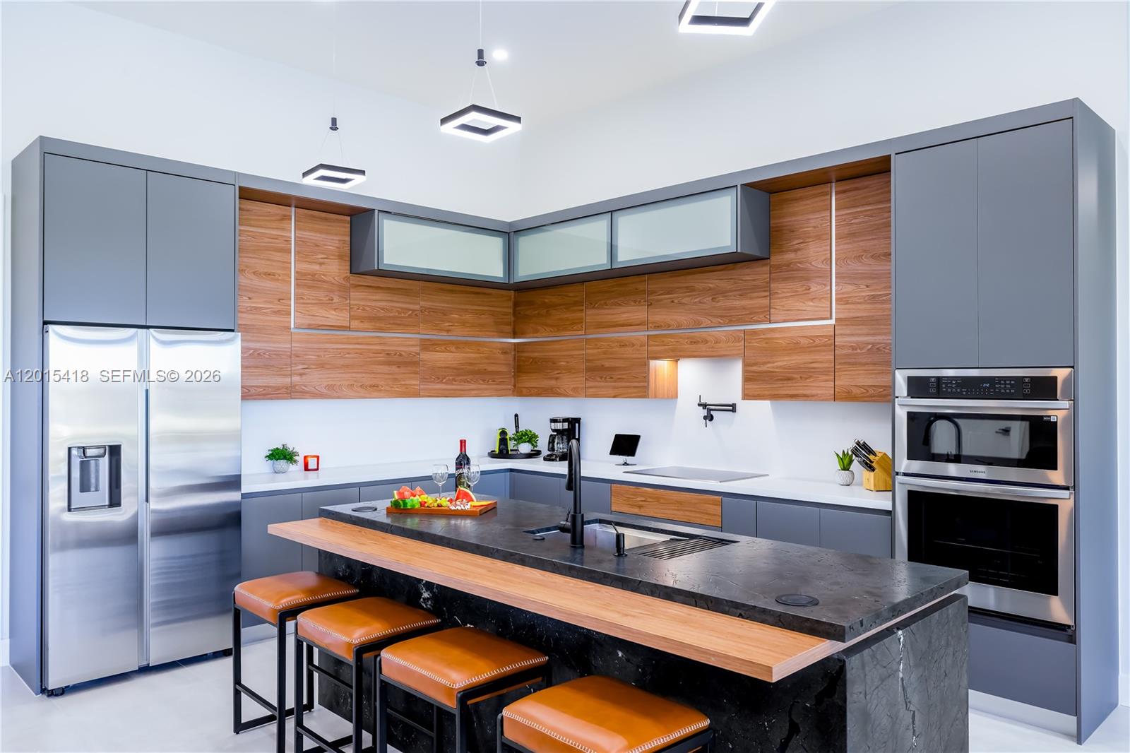 A modern kitchen features gray cabinets, wood-grain accents, a black stone island, and stainless appliances — 10 SW 33rd PL, Cape Coral FL 33904, CAPE CORAL, FL