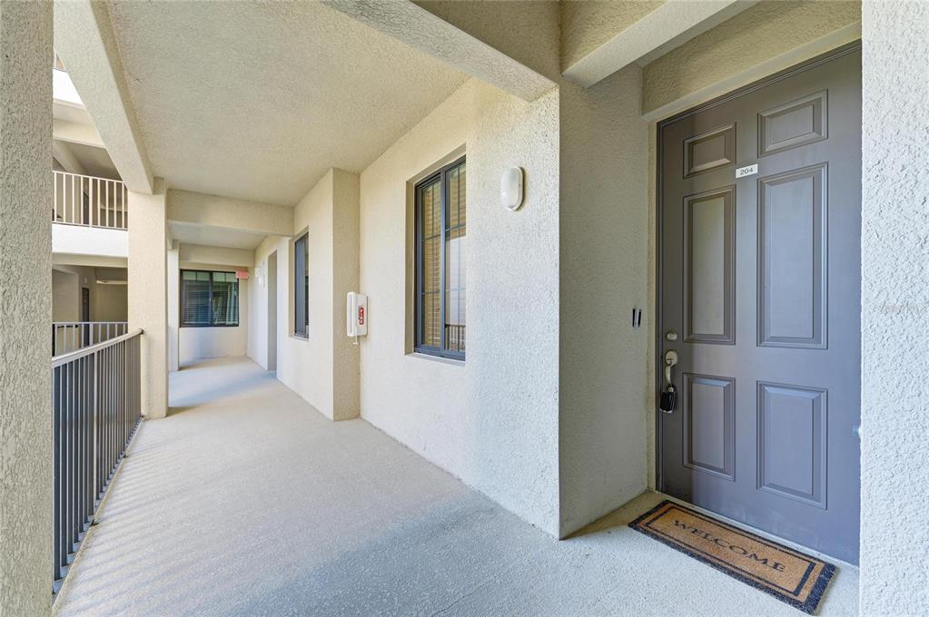 An exterior hallway leads to a gray apartment door labeled 204 with a welcome mat — 18114 GAWTHROP DRIVE UNIT 204, BRADENTON, FL