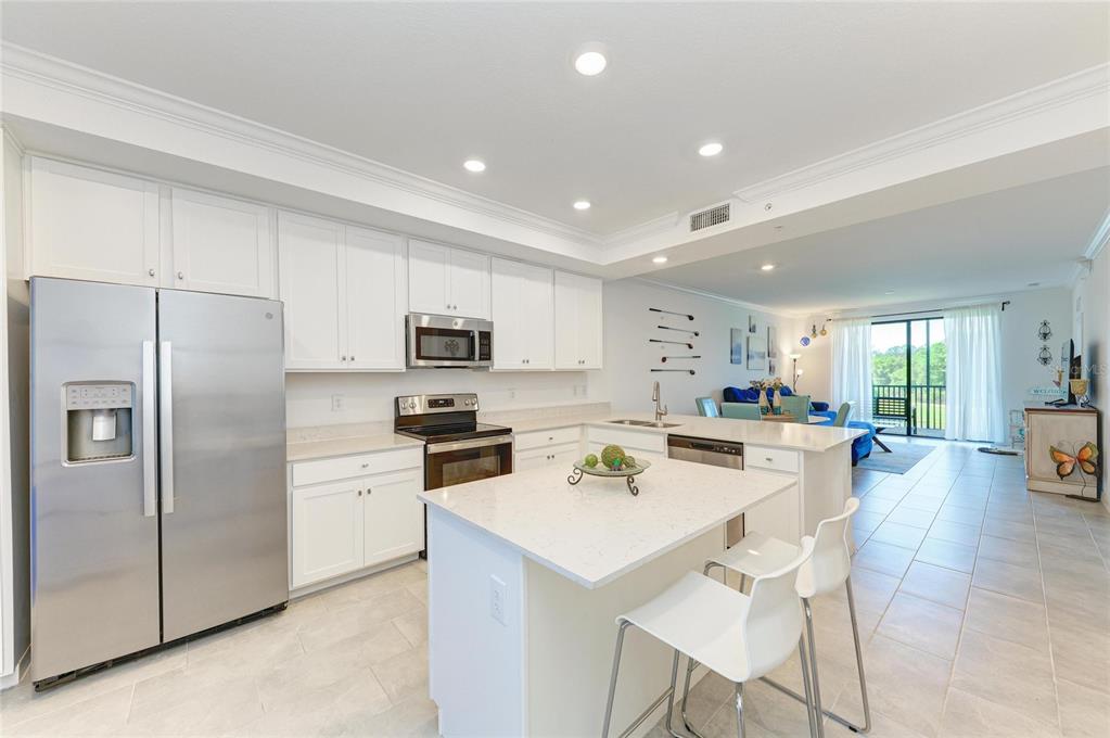 A kitchen with white cabinets, stainless steel appliances, and an island with two bar stools — 18114 GAWTHROP DRIVE UNIT 204, BRADENTON, FL