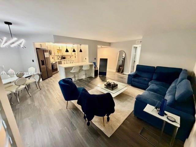 An open-concept living and dining area features a kitchen island, blue sofa, and modern lighting — 5800 CAMINO REAL # 306, Boca Raton FL 33433, BOCA RATON, FL