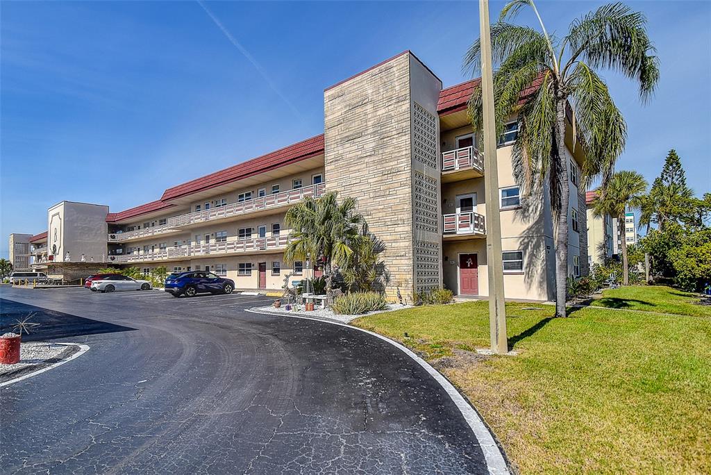 A multi-story apartment building with a parking lot and palm trees under a blue sky — 3010 59TH STREET S UNIT 301, GULFPORT, FL