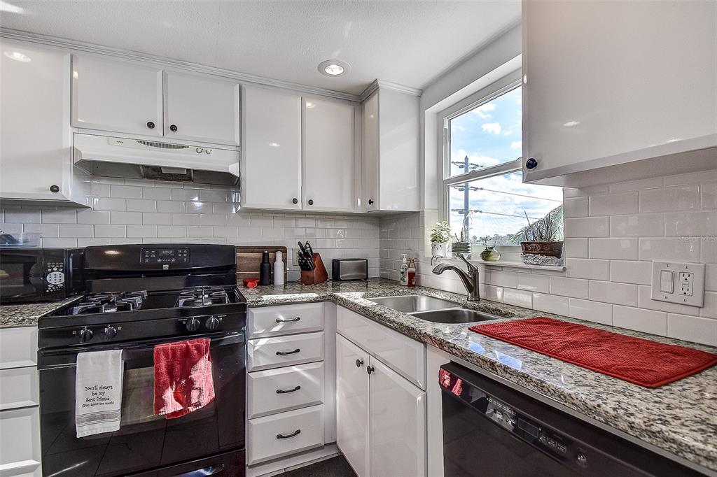 A kitchen features white cabinets, granite countertops, a black stove, and a subway tile backsplash — 3010 59TH STREET S UNIT 301, GULFPORT, FL