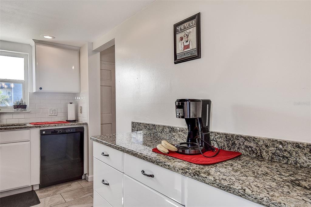 A kitchen features white cabinets, granite countertops, a coffee maker, and a framed wall print — 3010 59TH STREET S UNIT 301, GULFPORT, FL