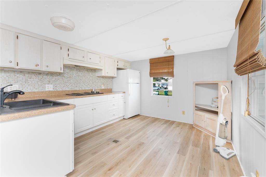 A kitchen with white cabinets, a mosaic backsplash, light wood flooring, and a white refrigerator — 7412 BECKLEY STREET, PORT CHARLOTTE, FL