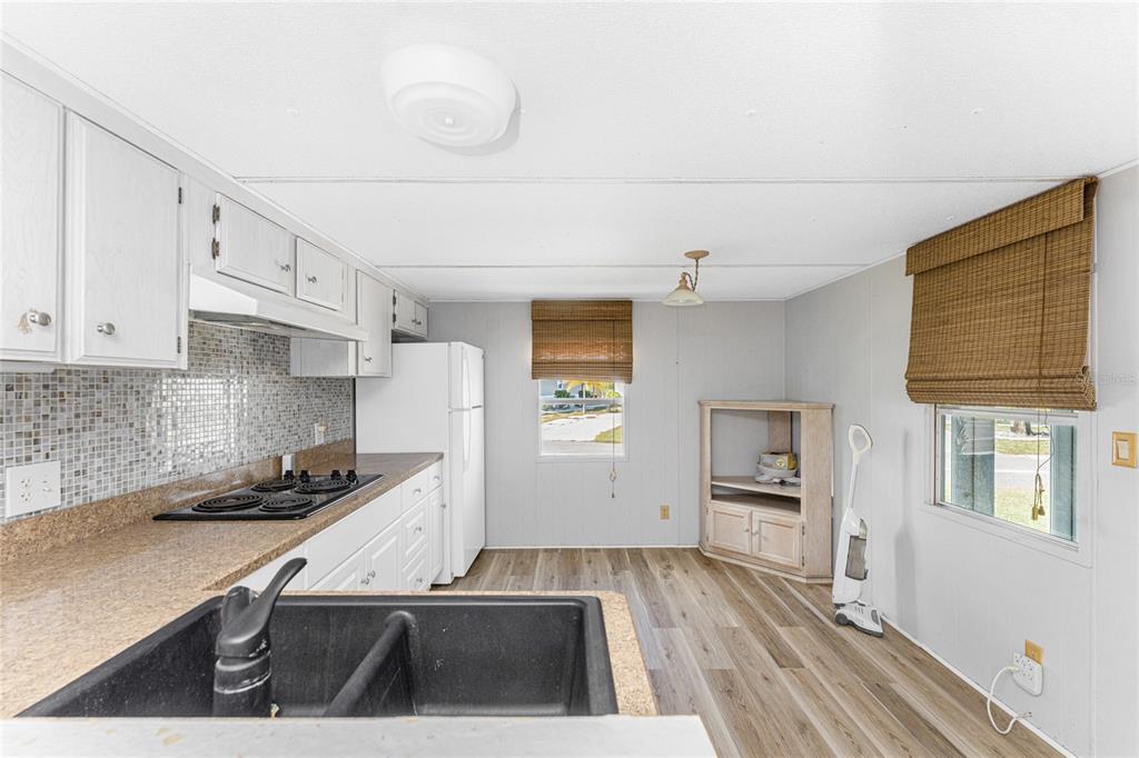 A kitchen with white cabinets, a mosaic tile backsplash, a black sink, and wood-look flooring — 7412 BECKLEY STREET, PORT CHARLOTTE, FL