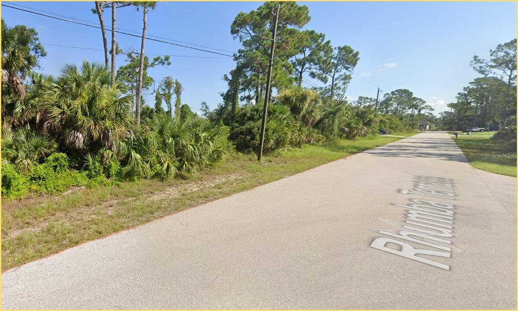 A paved road runs alongside a wooded lot with dense vegetation and tall pine trees — RHUMBA TERRACE Lot 30, NORTH PORT, FL