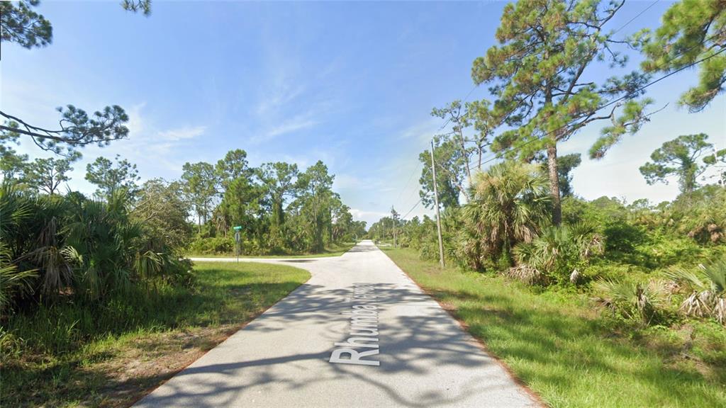 A paved road stretches through a wooded area with dense vegetation and tall pine trees — RHUMBA TERRACE Lot 30, NORTH PORT, FL