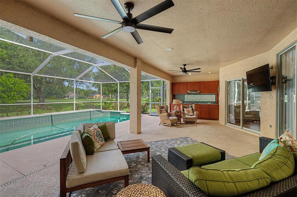 A covered patio features a swimming pool, outdoor kitchen, and seating area with ceiling fans — 1331 TRIMARAN PLACE, TRINITY, FL