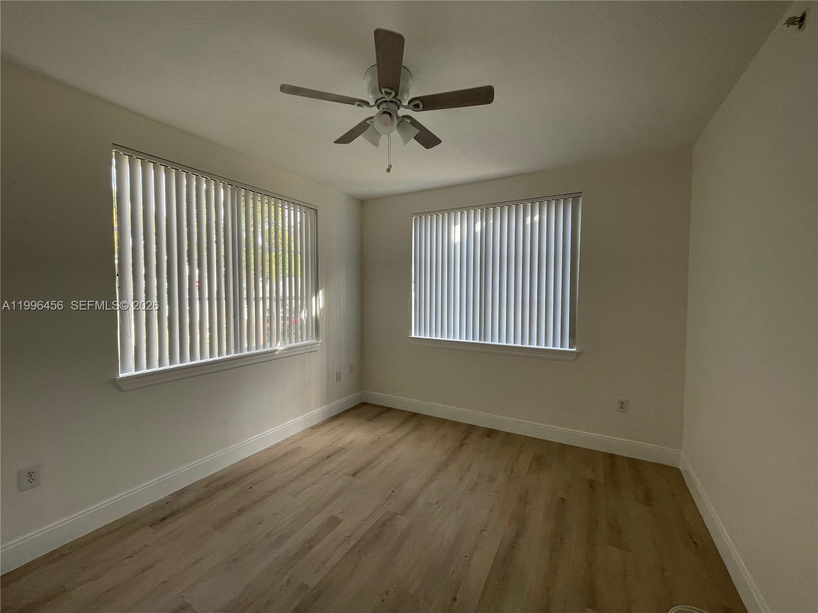 An empty room with light wood-look flooring, white walls, two windows with blinds, and a ceiling fan — 6851 SW 44th St # 210, Miami FL 33155, MIAMI, FL