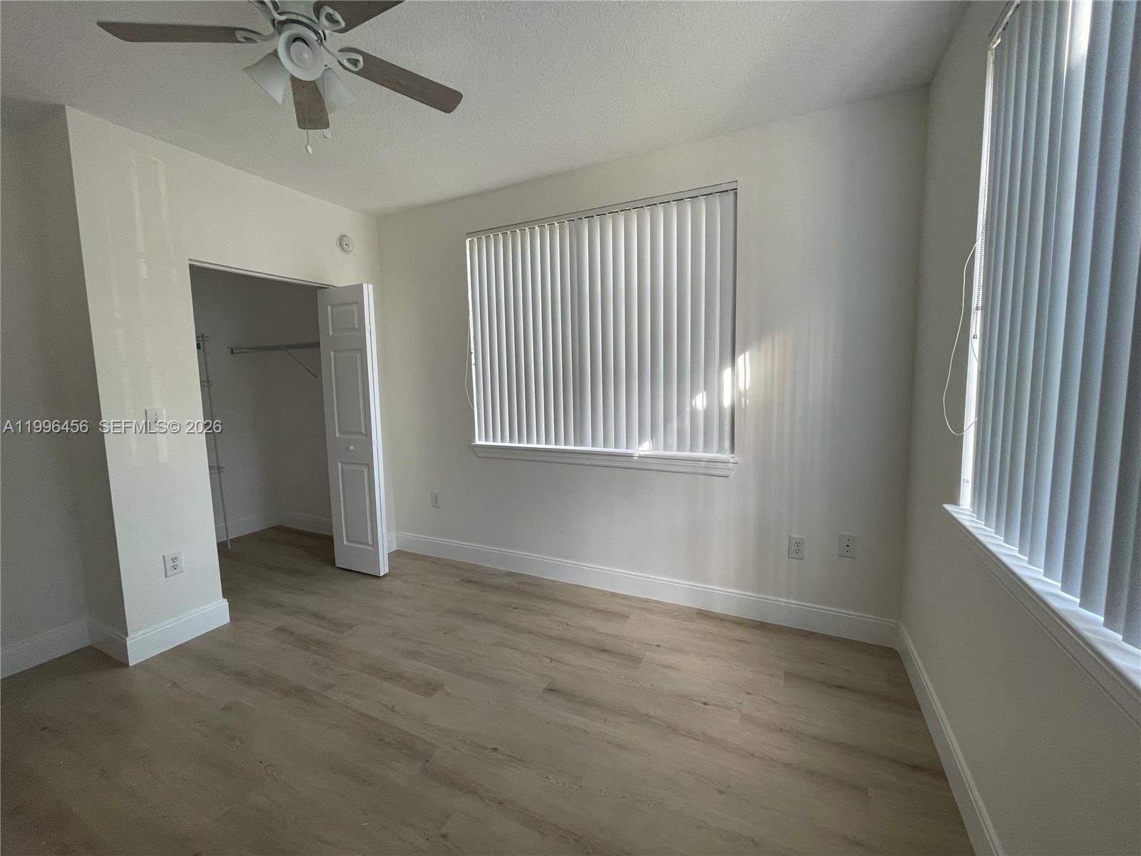 An empty bedroom features light wood-look flooring, white walls, a ceiling fan, and vertical blinds — 6851 SW 44th St # 210, Miami FL 33155, MIAMI, FL
