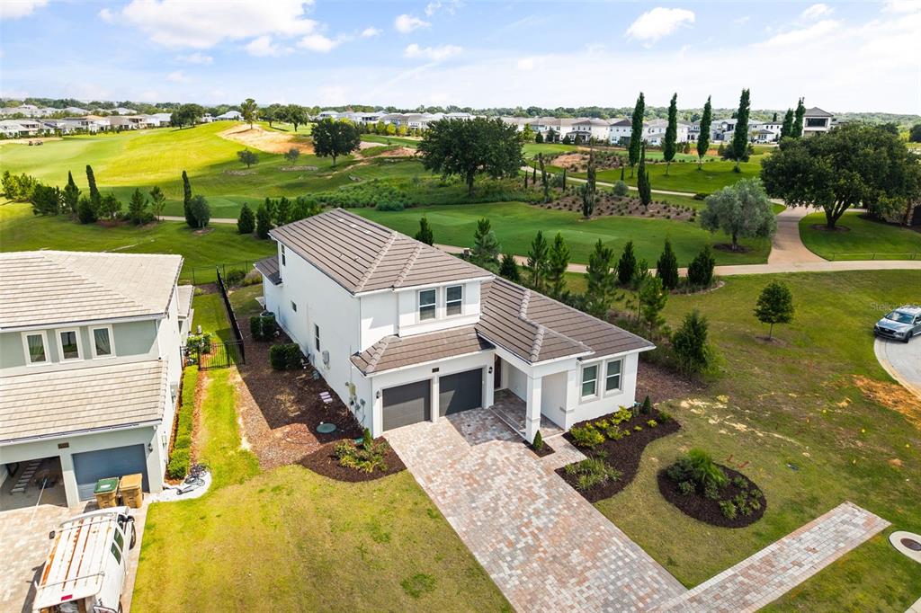 An aerial view of a two-story house with a paver driveway and golf course backdrop — 16000 VOLTERRA POINT, BELLA COLLINA, FL
