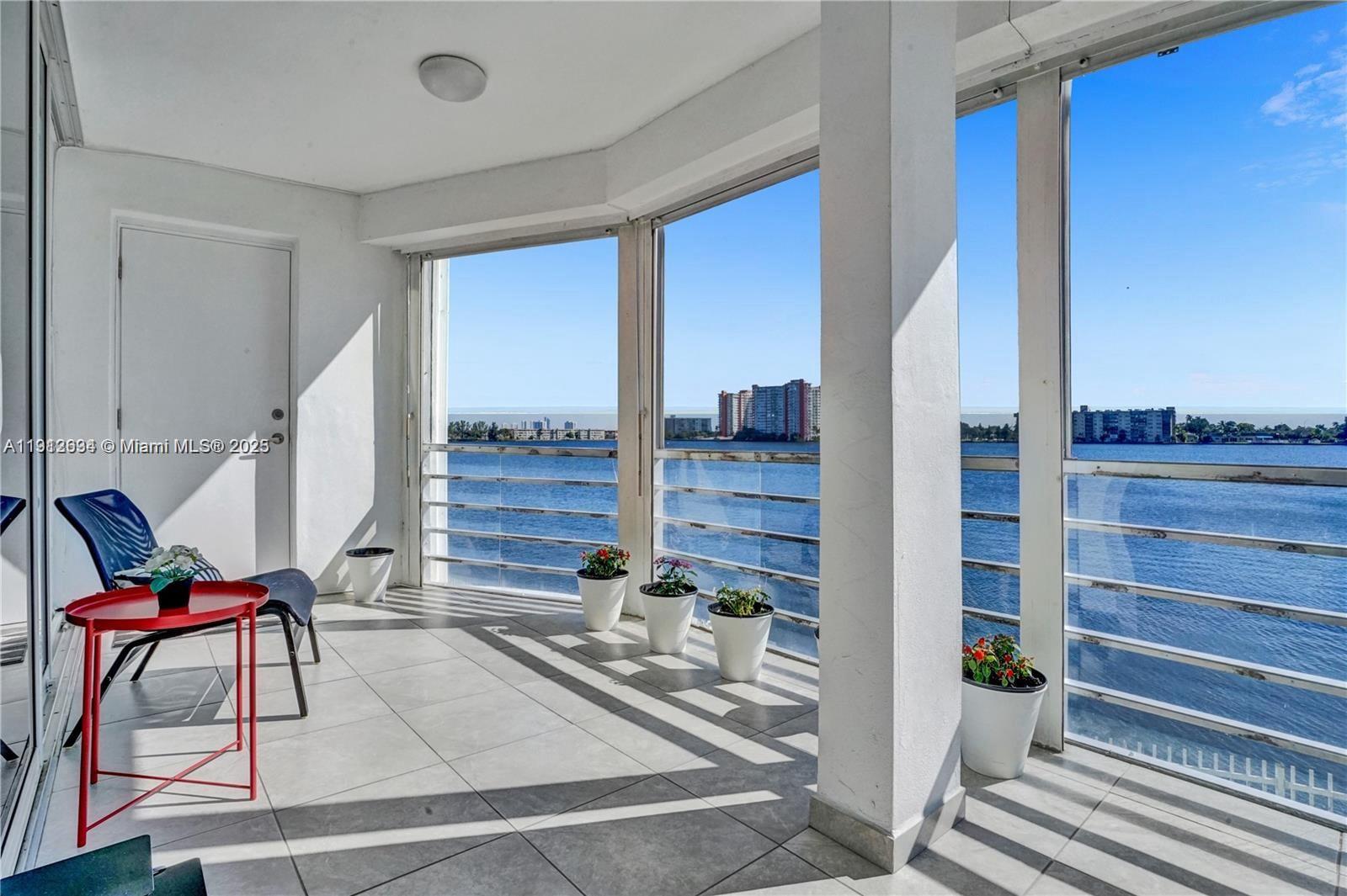 A balcony with tiled floors, potted plants, and a view of the water and buildings — 1000 NE 191st St # 21, Miami FL 33179, MIAMI, FL
