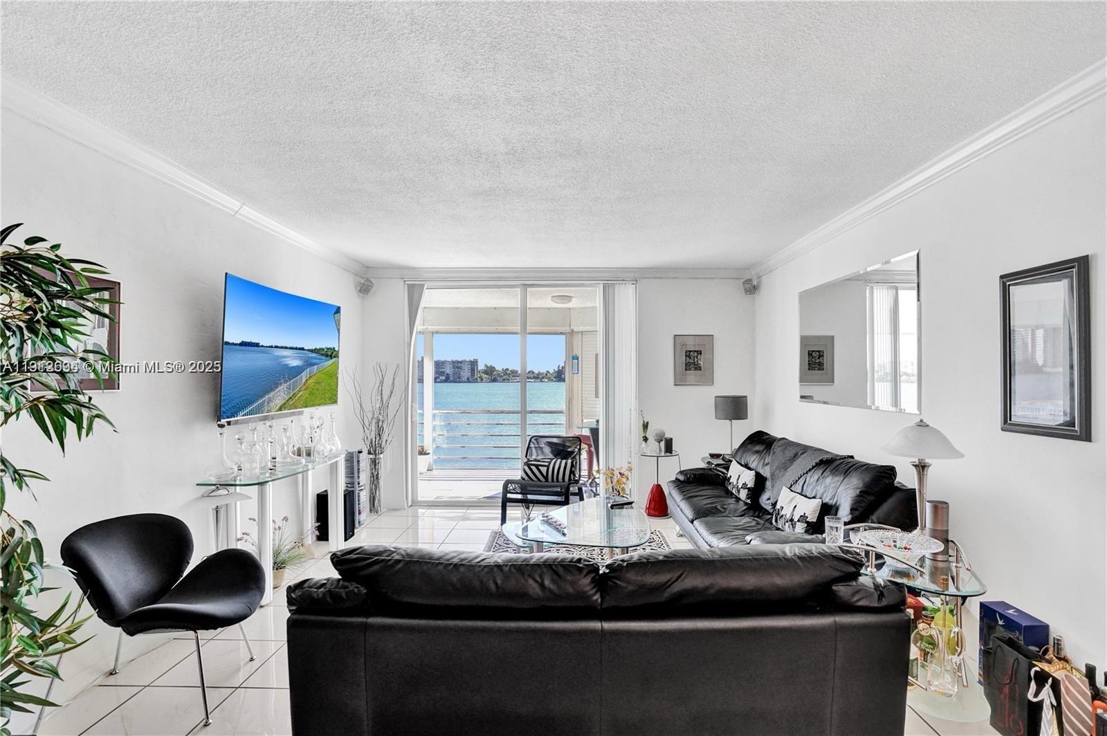 A living room with white tile floors, black leather sofas, and a balcony overlooking water — 1000 NE 191st St # 21, Miami FL 33179, MIAMI, FL