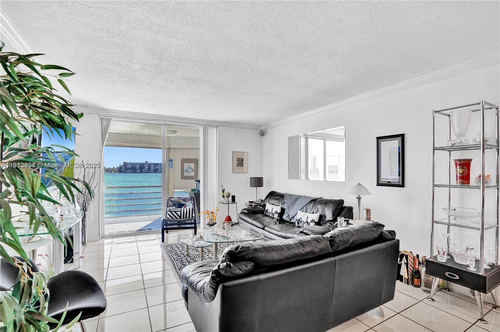 A living room with white tile floors, a black leather sofa, and a balcony overlooking water — 1000 NE 191st St # 21, Miami FL 33179, MIAMI, FL