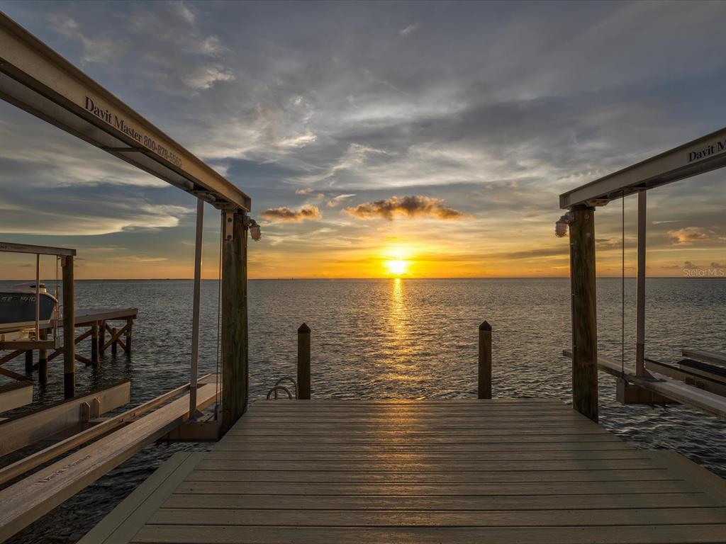A wooden dock with railings extends over the water toward a boat lift and horizon — 5101 WESTSHORE DRIVE, NEW PORT RICHEY, FL