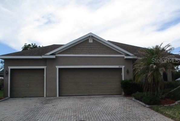 A single-story house exterior features a three-car garage and a paved driveway under a cloudy sky — 3827 SPIRITED CIRCLE, ST CLOUD, FL